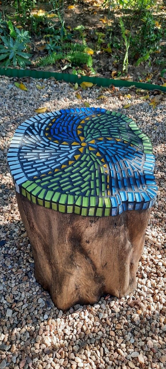 a piece of wood sitting on top of a gravel covered ground next to trees and bushes