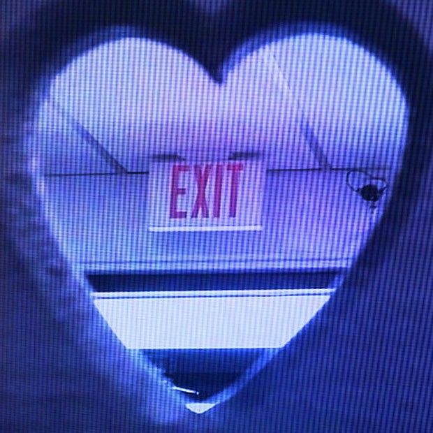 an exit sign is seen through a heart - shaped hole in the wall behind it