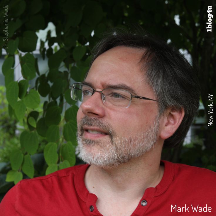 a man wearing glasses and a red shirt is looking off into the distance with trees in the background