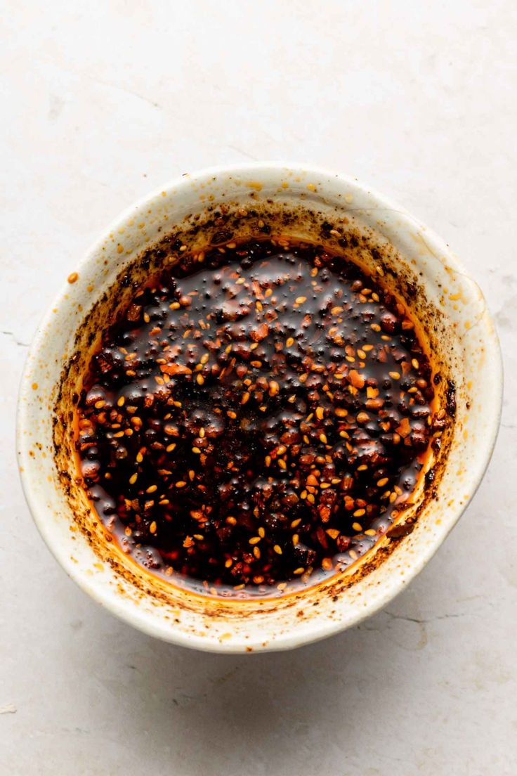 a white bowl filled with black sauce on top of a marble countertop next to a knife