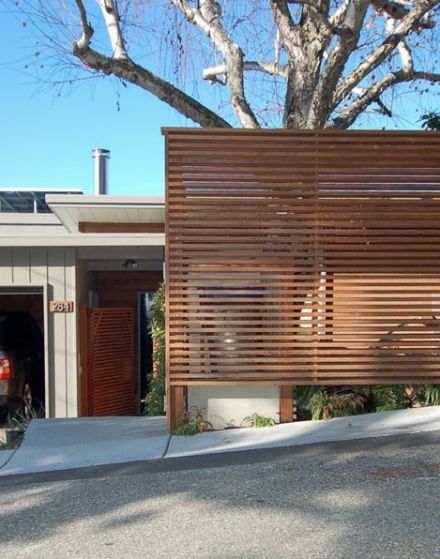 a large wooden slatted screen on the side of a building next to a tree