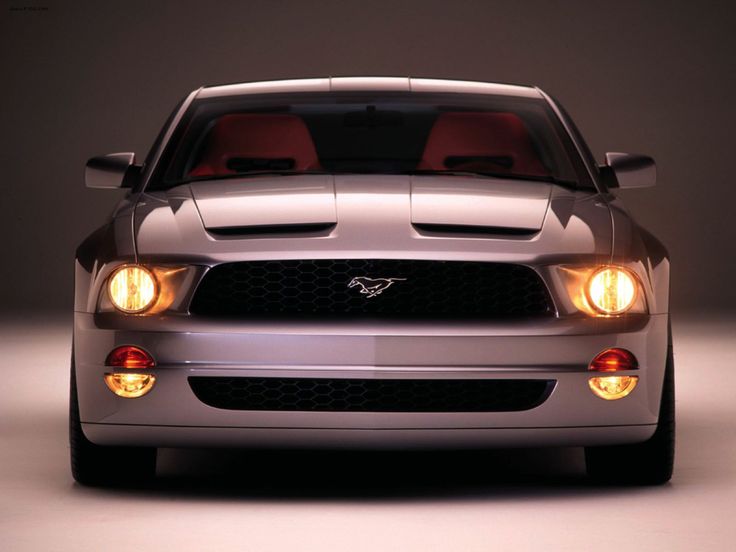 the front end of a silver mustang car with its lights on and headlamps down