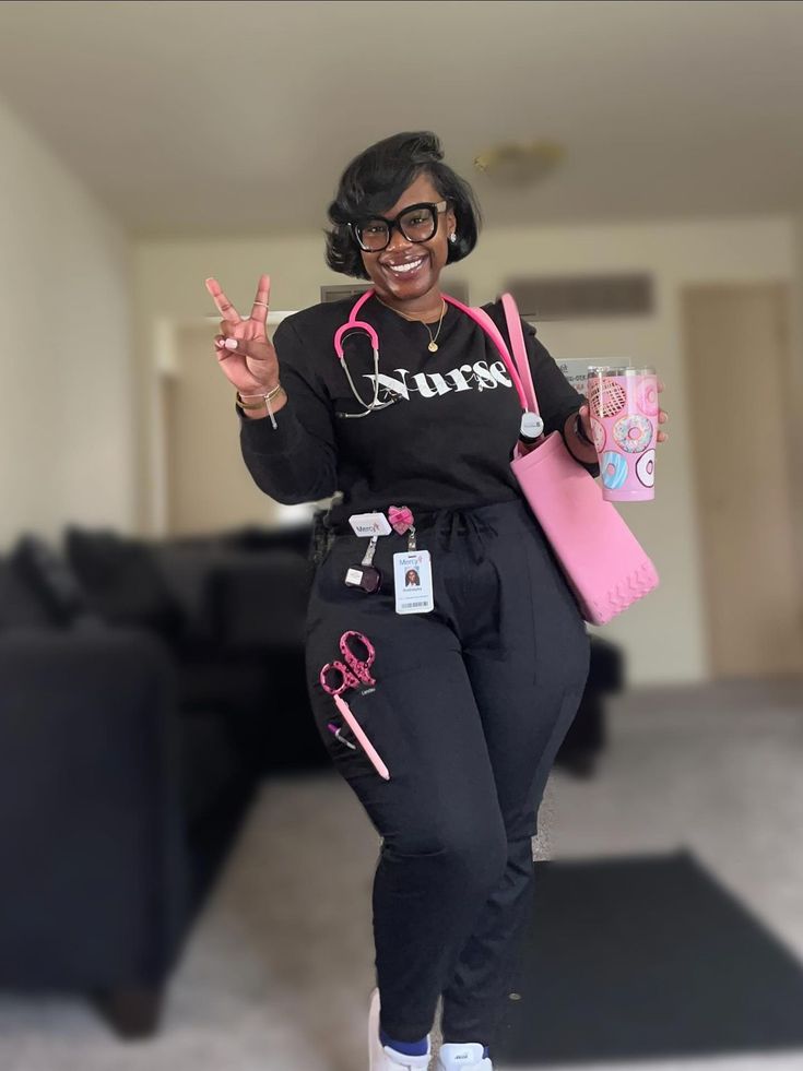 a woman in black and pink outfit holding up two fingers while standing next to a couch