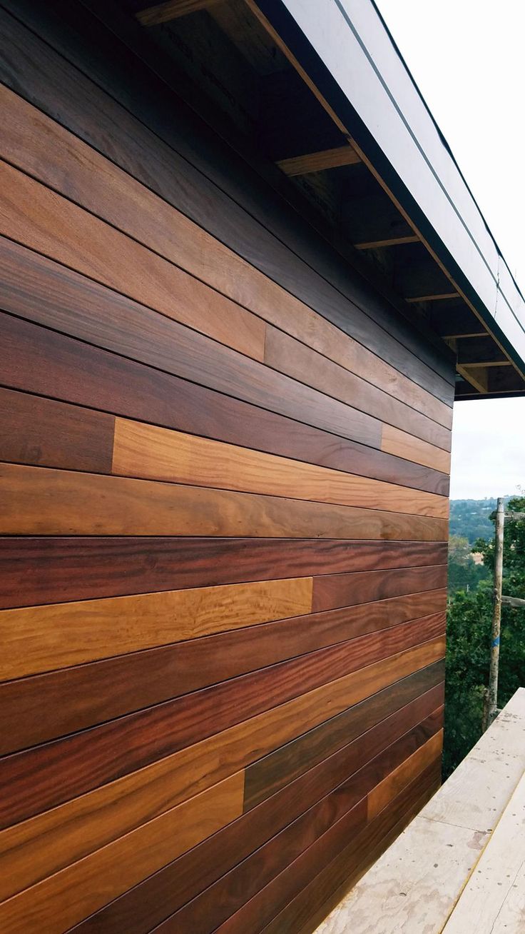 the side of a building with wood siding on it's sides and trees in the background