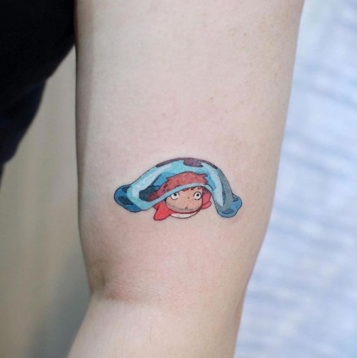 a woman's arm with a cartoon character tattoo on the left side of her arm