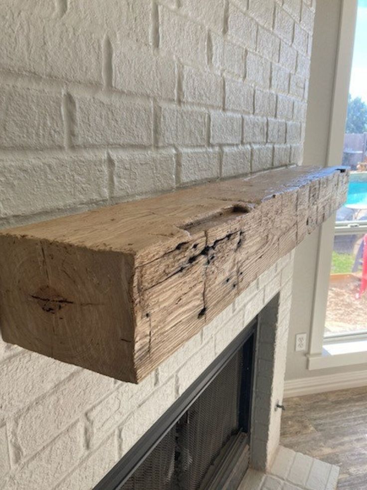 a fireplace mantle made out of wood with a brick wall in the background and an open window