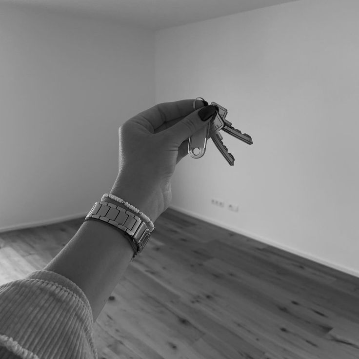 a person holding two keys in the middle of a room with wood floors and white walls