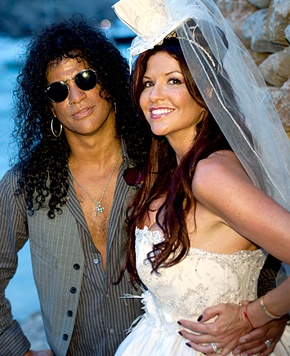 two people standing next to each other in front of a stone wall with water behind them