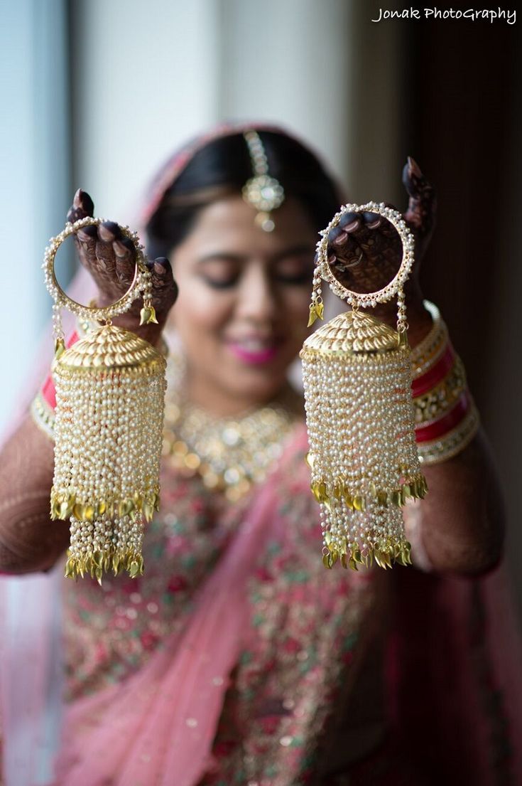 a woman in a pink sari holding two gold earrings