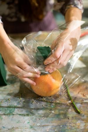 a person is peeling an orange on a table with plastic wrap around it's edges