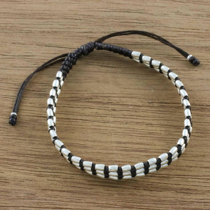 two white and black beads are on a brown leather cord with a silver clasp that is attached to an adjustable bracelet