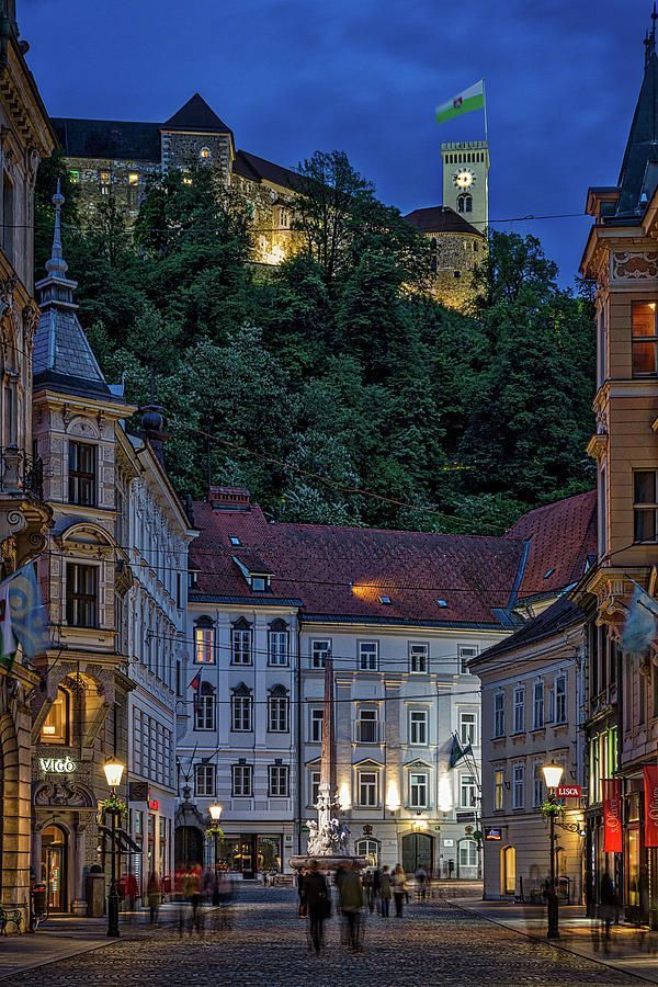 people are walking down the cobblestone street in front of old buildings at night