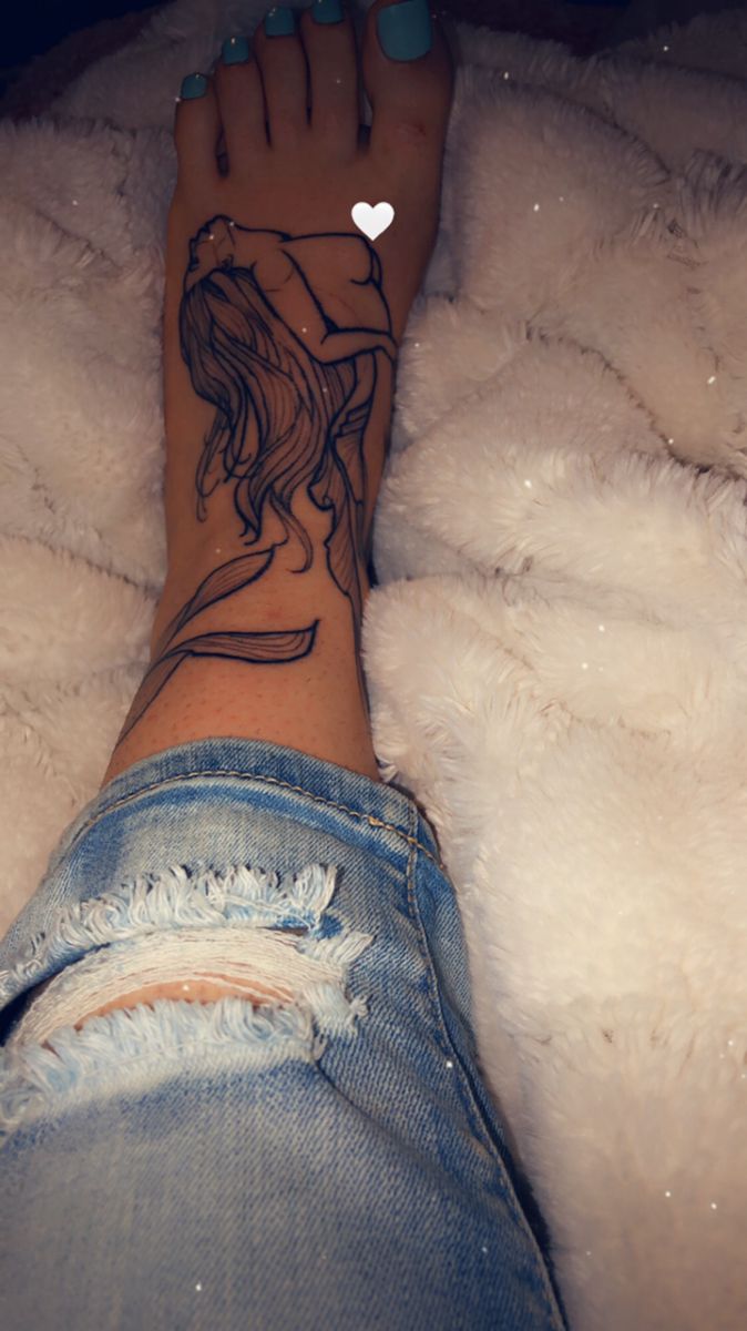 a woman's foot with a tattoo on it sitting on top of a fluffy white blanket