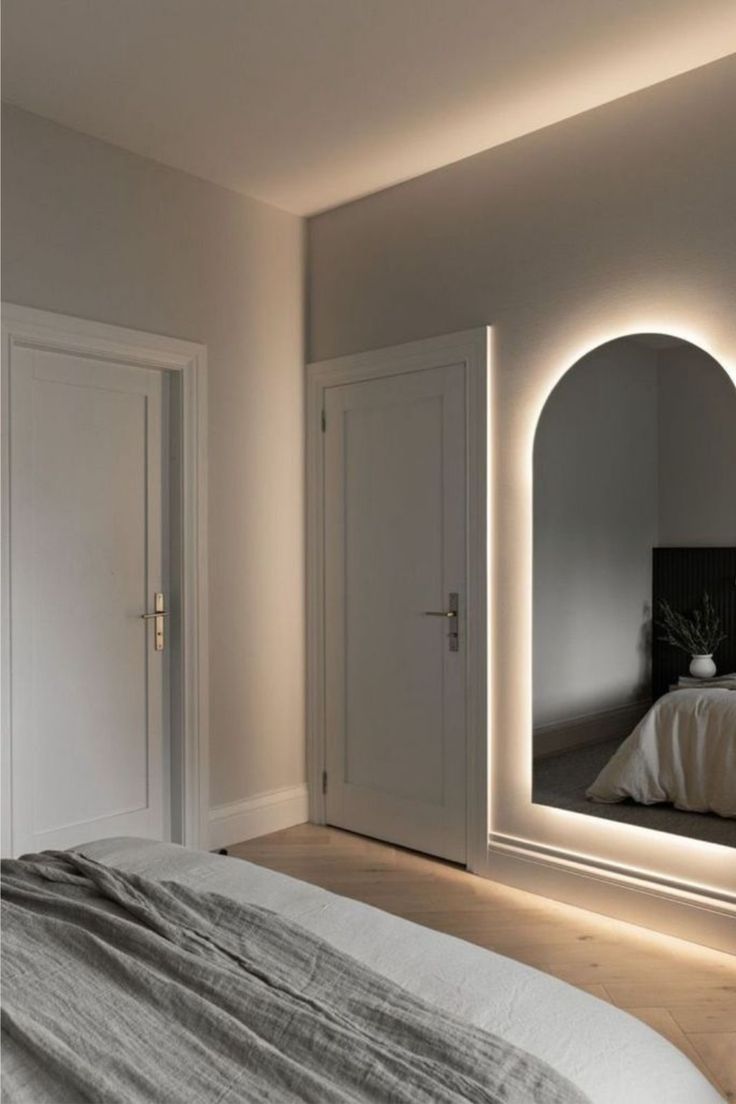 a white bed sitting under a large mirror in a bedroom next to a doorway and closet