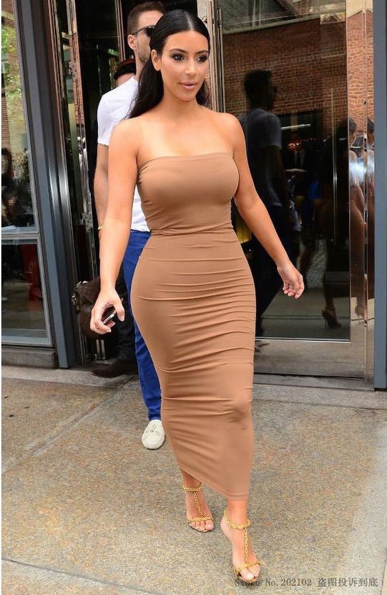 a woman in a tan dress is walking down the street with her hand on her hip