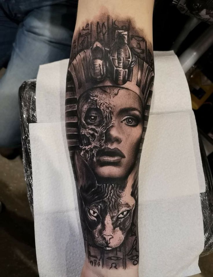 a woman's arm with an egyptian mask on it and two cats in the background