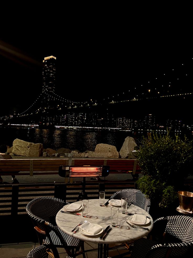 an outdoor dining area with tables and chairs overlooking the water at night time, lit up by street lights