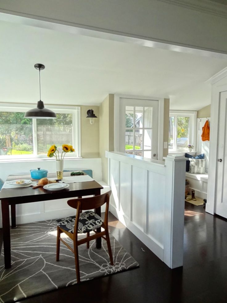 a dining room table and chairs in front of a window with white paneling on the walls