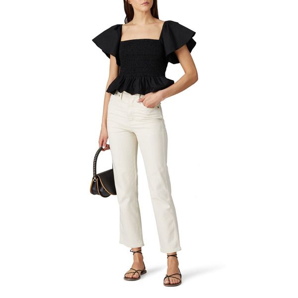 a woman in white pants and black top holding a handbag with her right hand