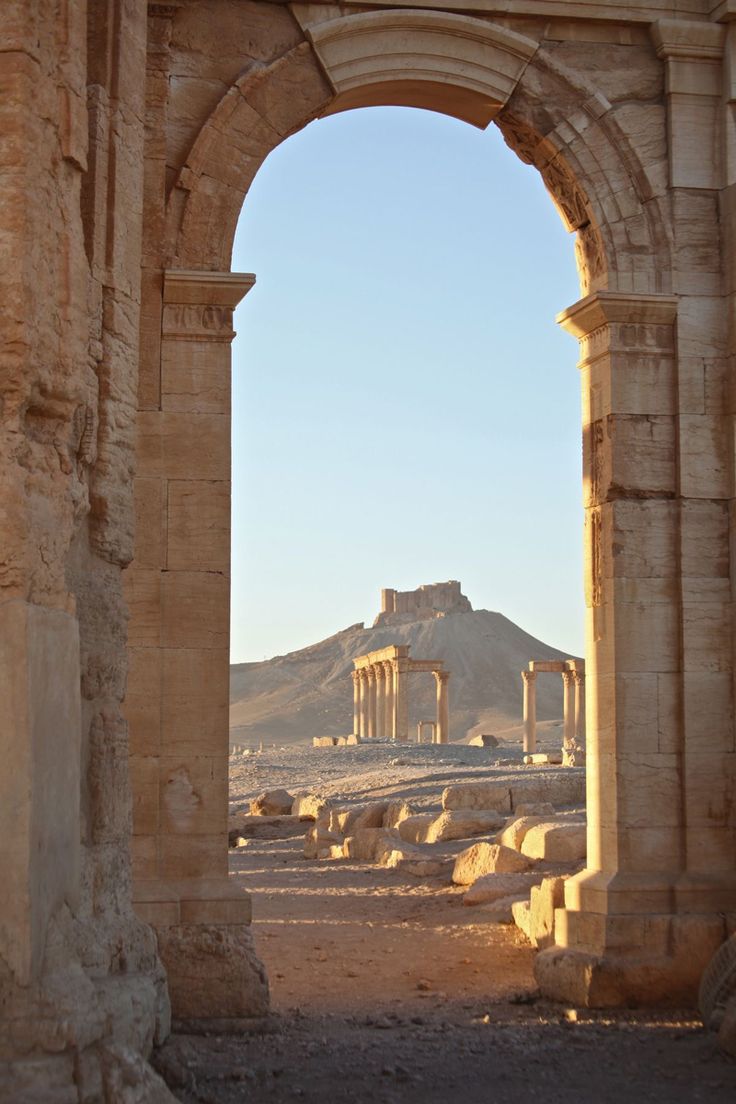 an arch in the middle of a desert area with mountains in the backgroud