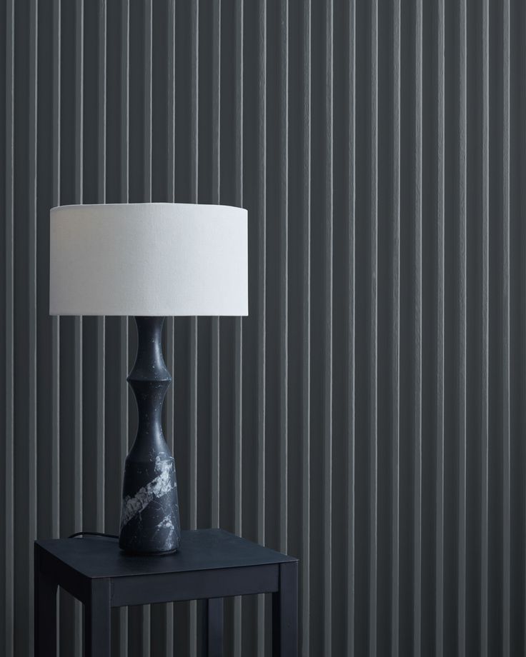 a black table lamp with a white shade on it in front of a striped wall