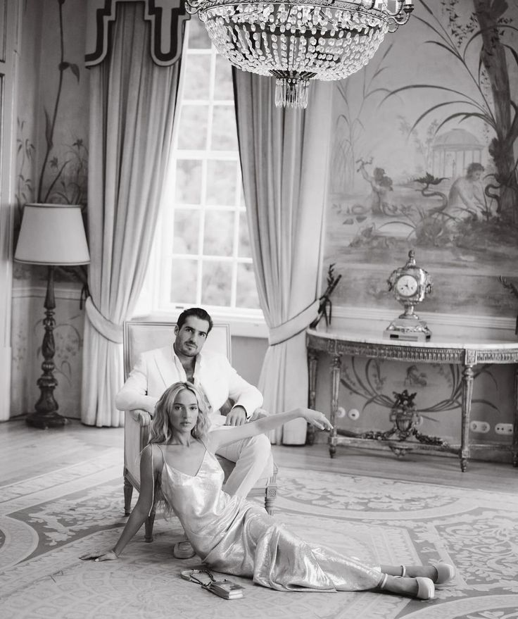 a man and woman sitting on the floor in front of a chandelier, posing for a black and white photo