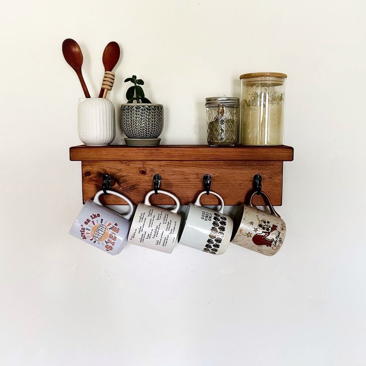 three mugs are hanging on a shelf with spoons