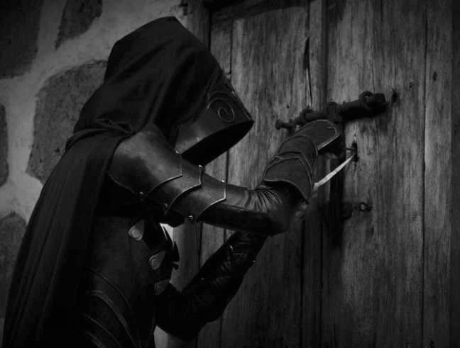 black and white photograph of a person in costume holding onto a door with a knife