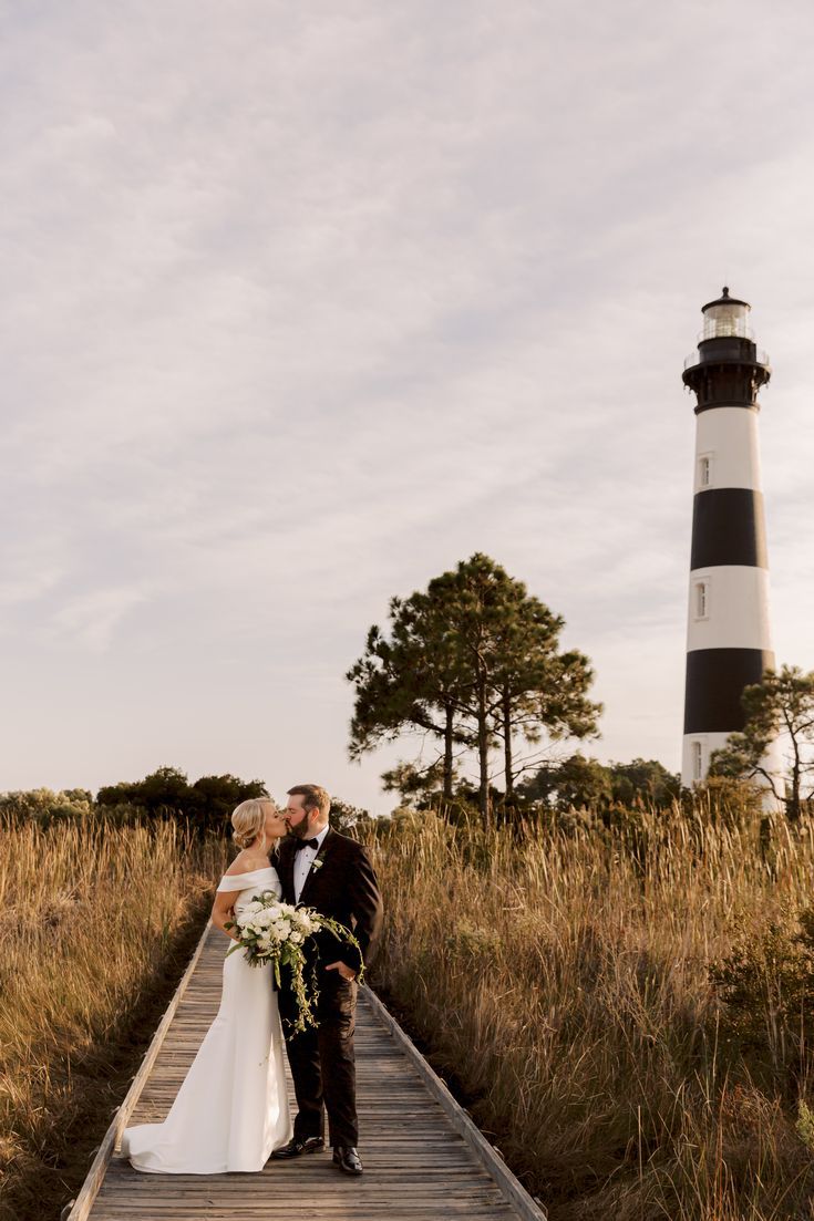 a bride and groom standing on a dock in front of a lighthouse