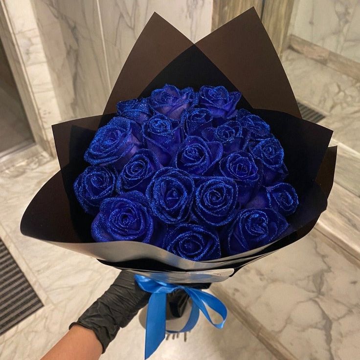 a bouquet of blue roses wrapped in black paper and tied with a blue ribbon is being held by someone's hand