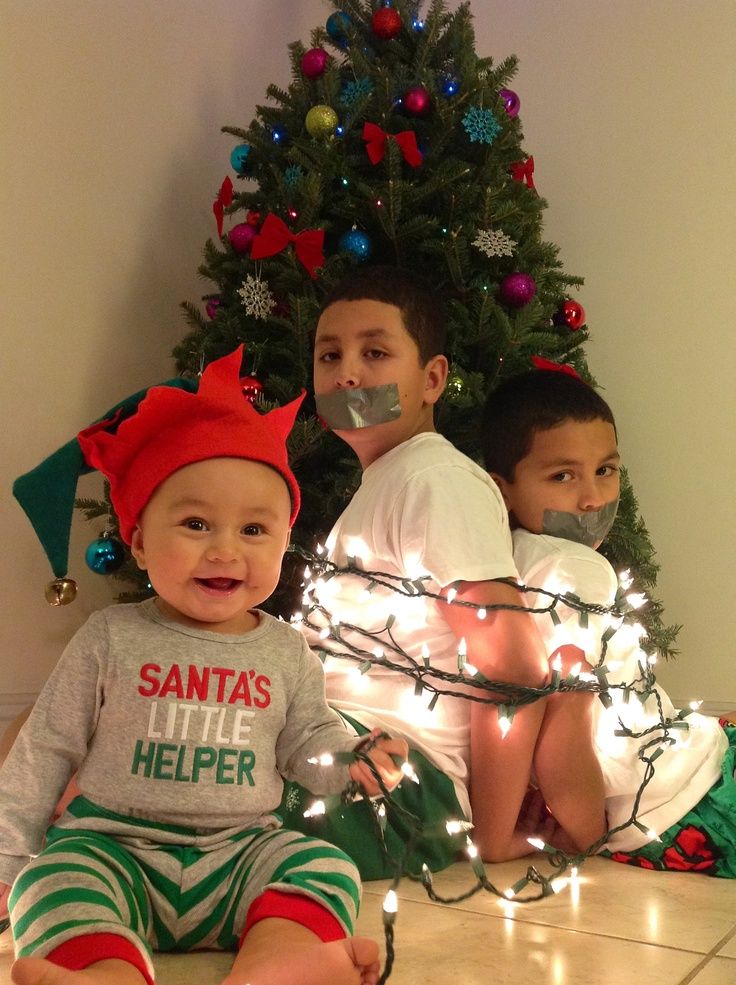 two young boys sitting on the floor in front of a christmas tree with lights around them