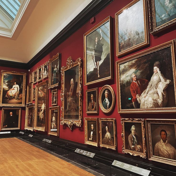 a room filled with lots of paintings on the wall and wooden floored floors in front of red walls