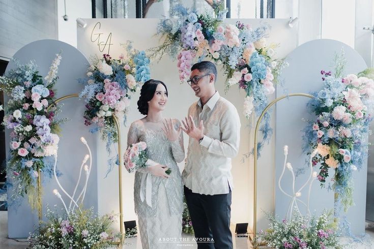 a man and woman standing next to each other in front of a flower covered wall