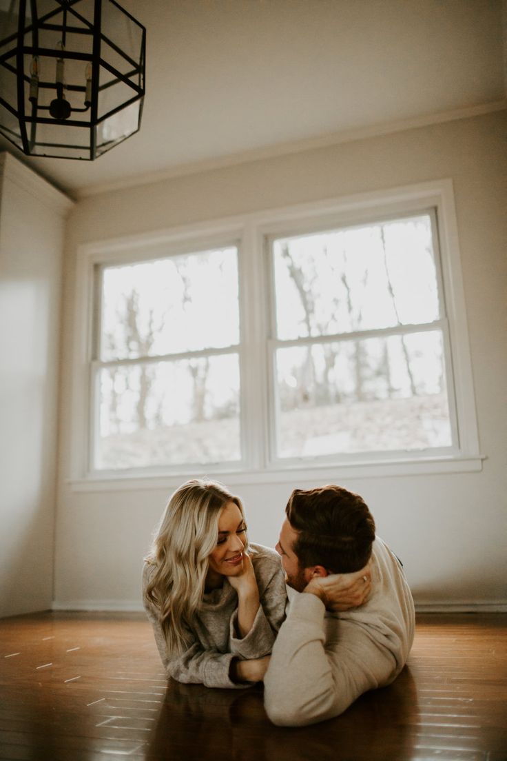 a man and woman sitting on the floor in front of two windows, one holding his head