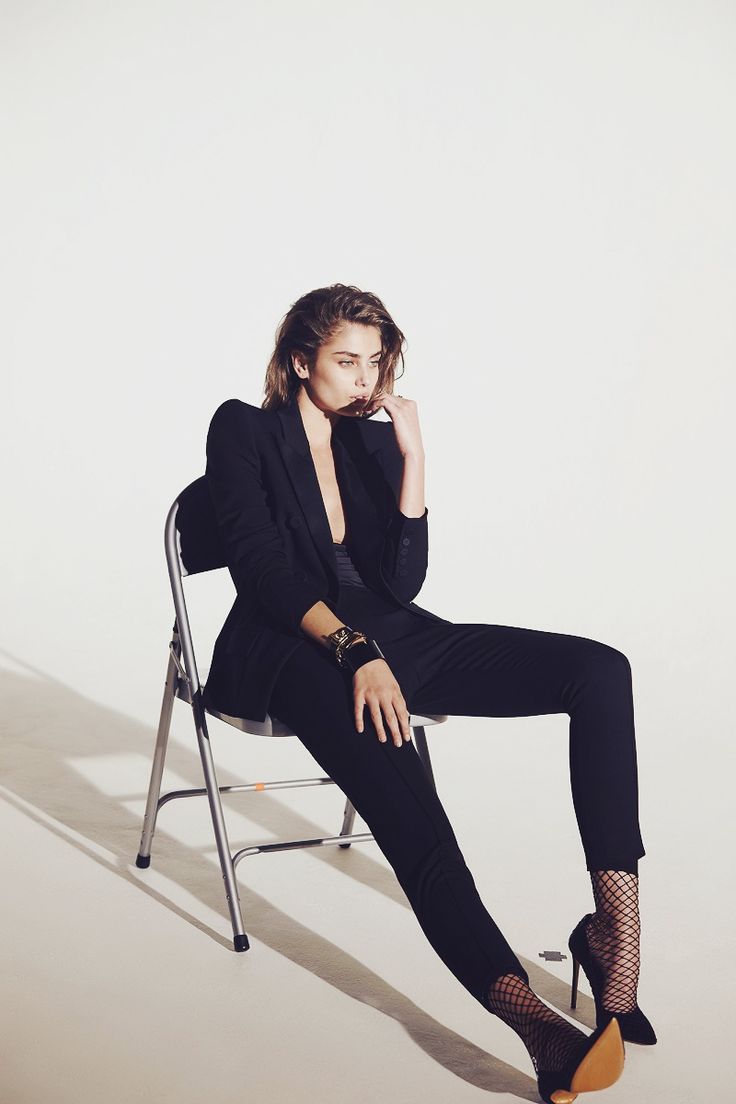 a woman sitting in a chair with her legs crossed and wearing black clothing, posing for the camera