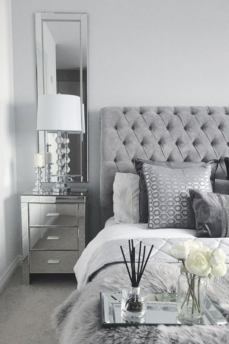 a bedroom with a bed, mirror and flowers in vases on the end table