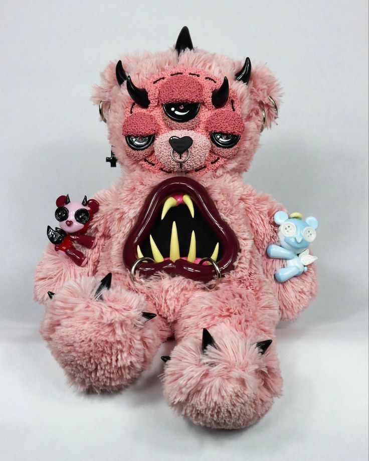 a pink teddy bear with fangs on it's face and mouth is holding a toy