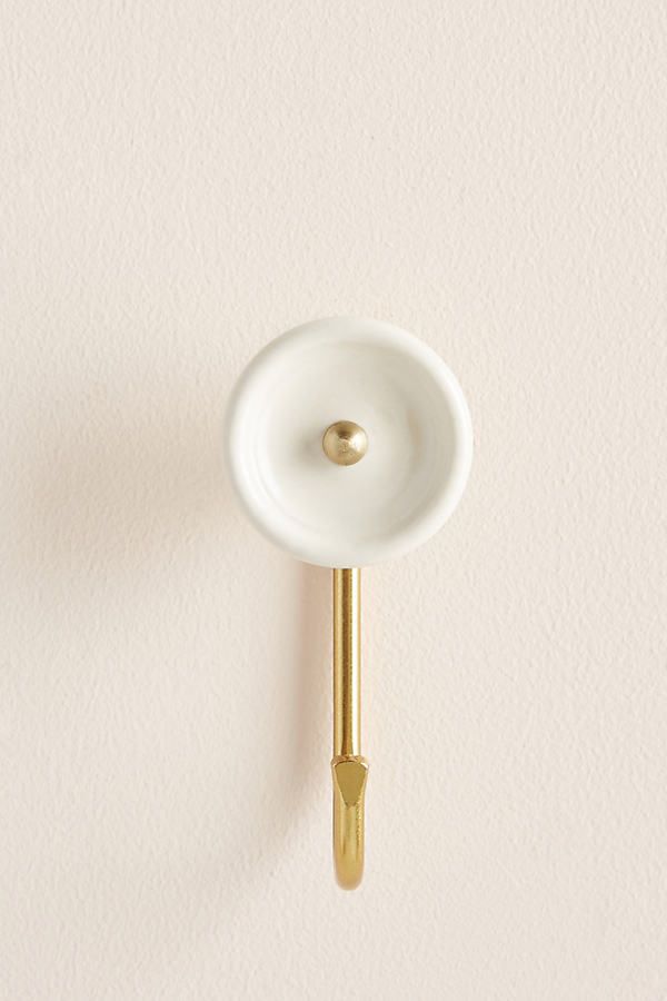 a white and gold hook on a wall with a light beige paint color behind it