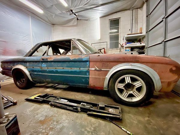 an old, rusted car in a garage with other tools and equipment around it