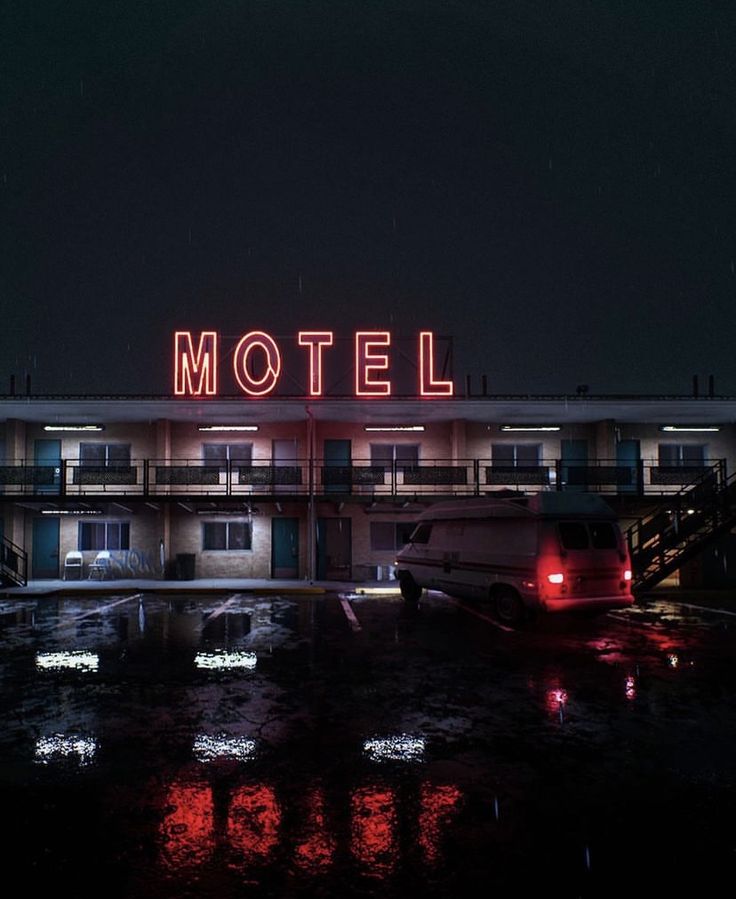 a motel lit up at night with the word motel on it's roof and cars parked in front