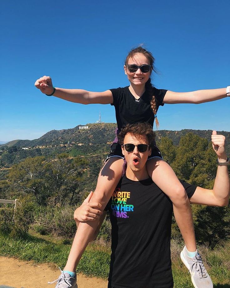 two people standing on top of each other with their arms in the air and one person wearing sunglasses