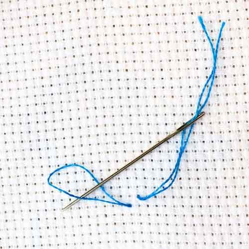 the needle is hooked up to thread on the white fabric with blue yarn around it