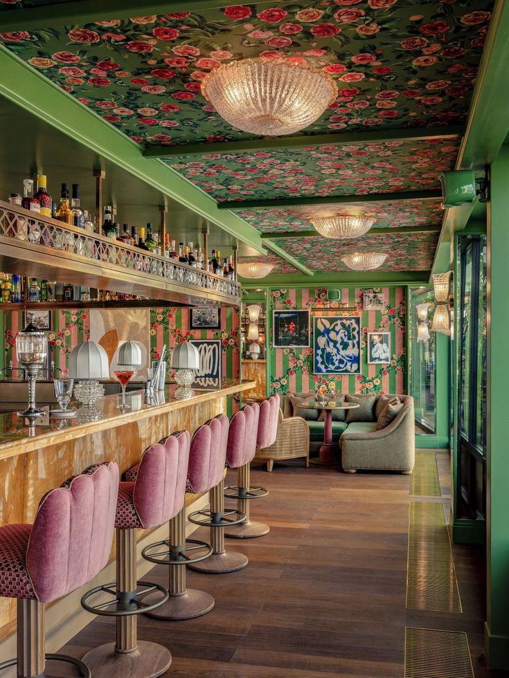 the bar is decorated with floral wallpaper and pink velvet stools in front of it