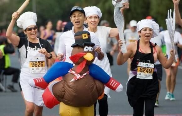 a group of people in costumes running down a street with balloons and an inflatable turkey