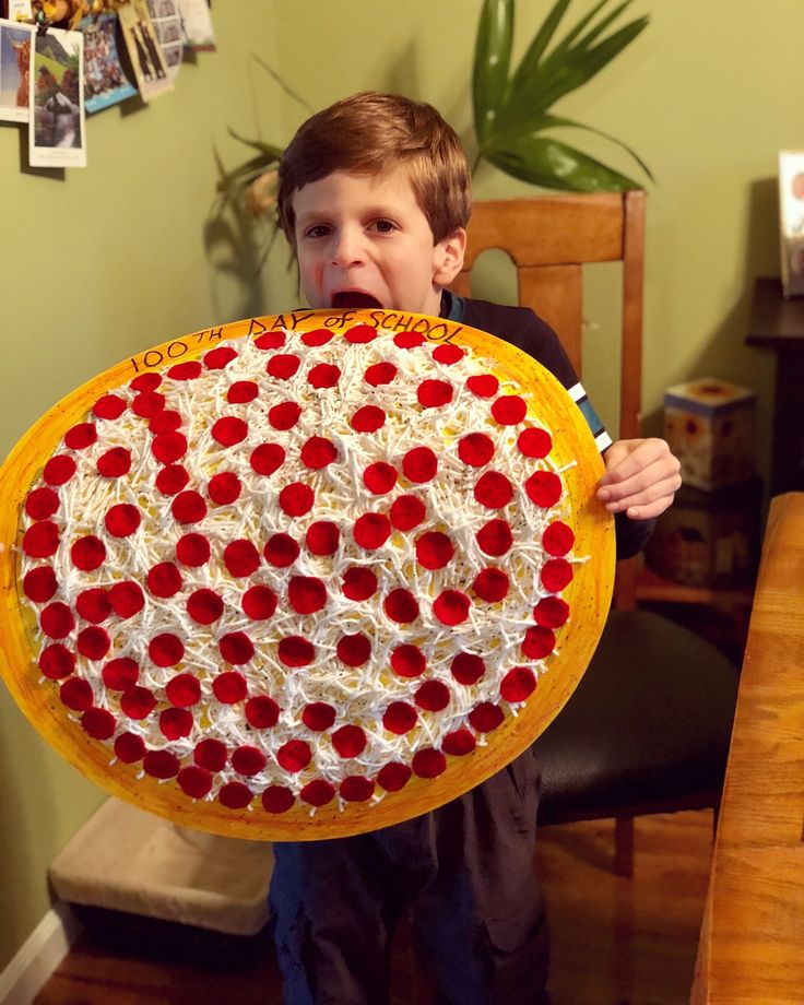 a young boy holding up a large pizza