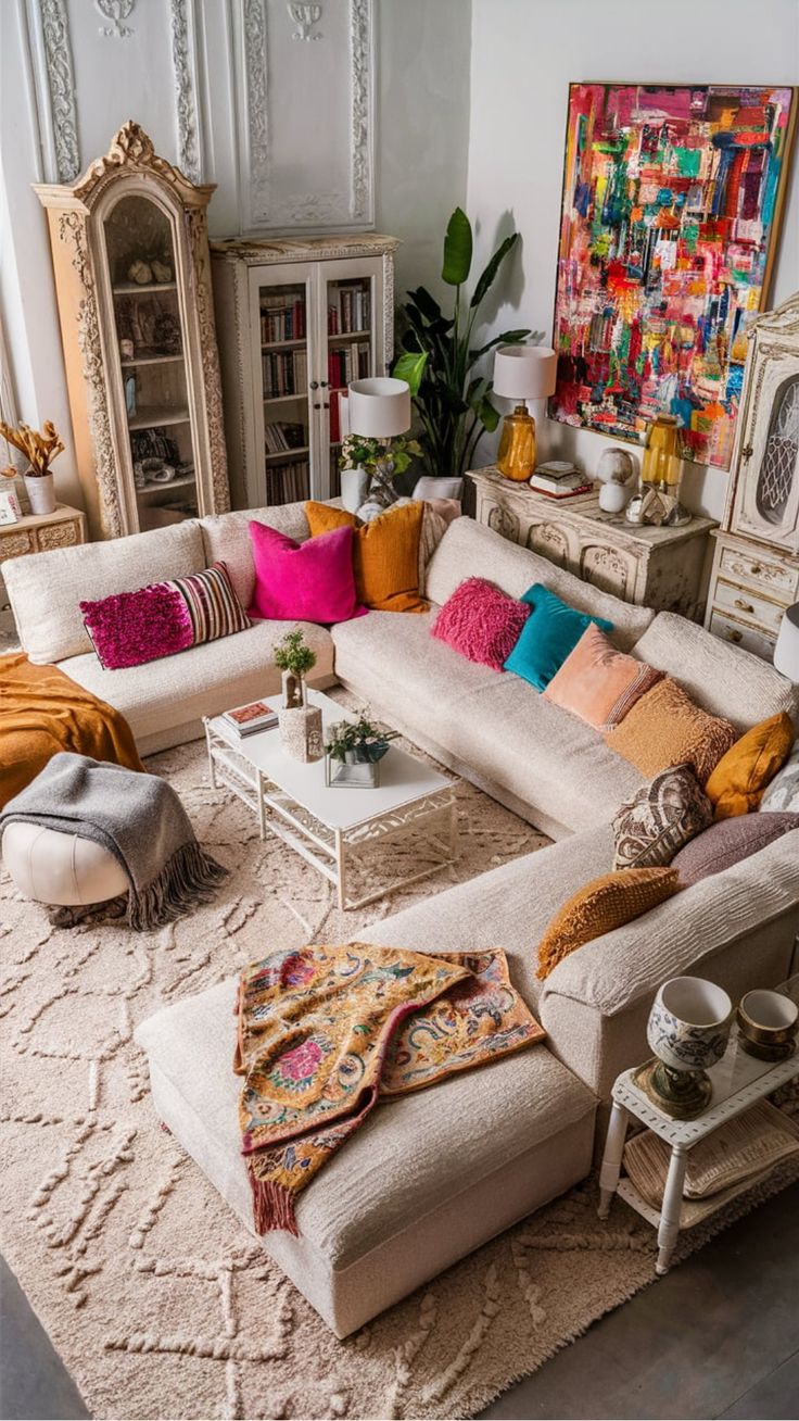 Cozy living room with a large L-shaped sofa adorned with colorful throw pillows, a vibrant abstract painting on the wall, and decorative plants. Double Rug Living Room Bohemian, Beige Couch Boho Living Room, Bohemian Seating Area, Boho Chic Living Room Moroccan Style, Retro Boho Living Room, Living Room Moroccan Style, Boho Glam Living Room, Cream Couch Living Room, Cultural Decor