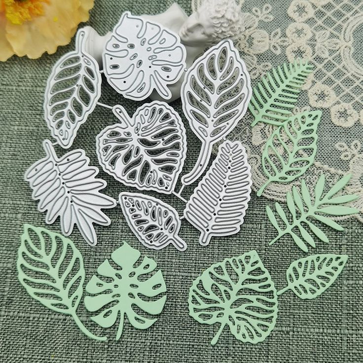 paper cut outs with leaves and laces on a green tablecloth next to flowers