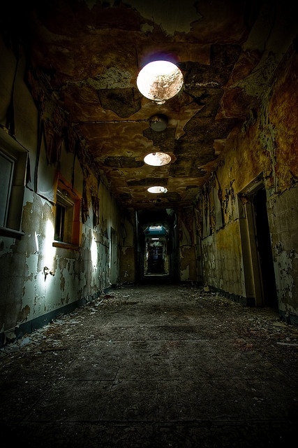 an empty hallway with peeling paint on the walls and lights hanging down from the ceiling