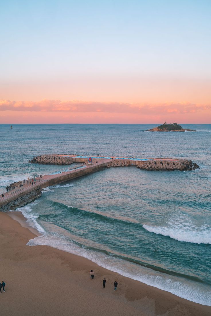 people are walking along the beach at sunset