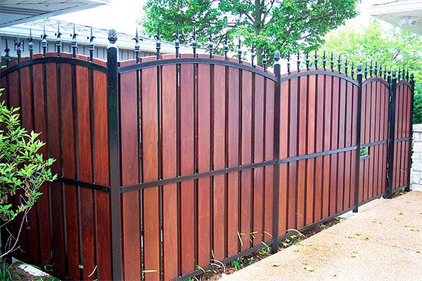 a wooden fence that is next to a tree and shrubbery in front of a house